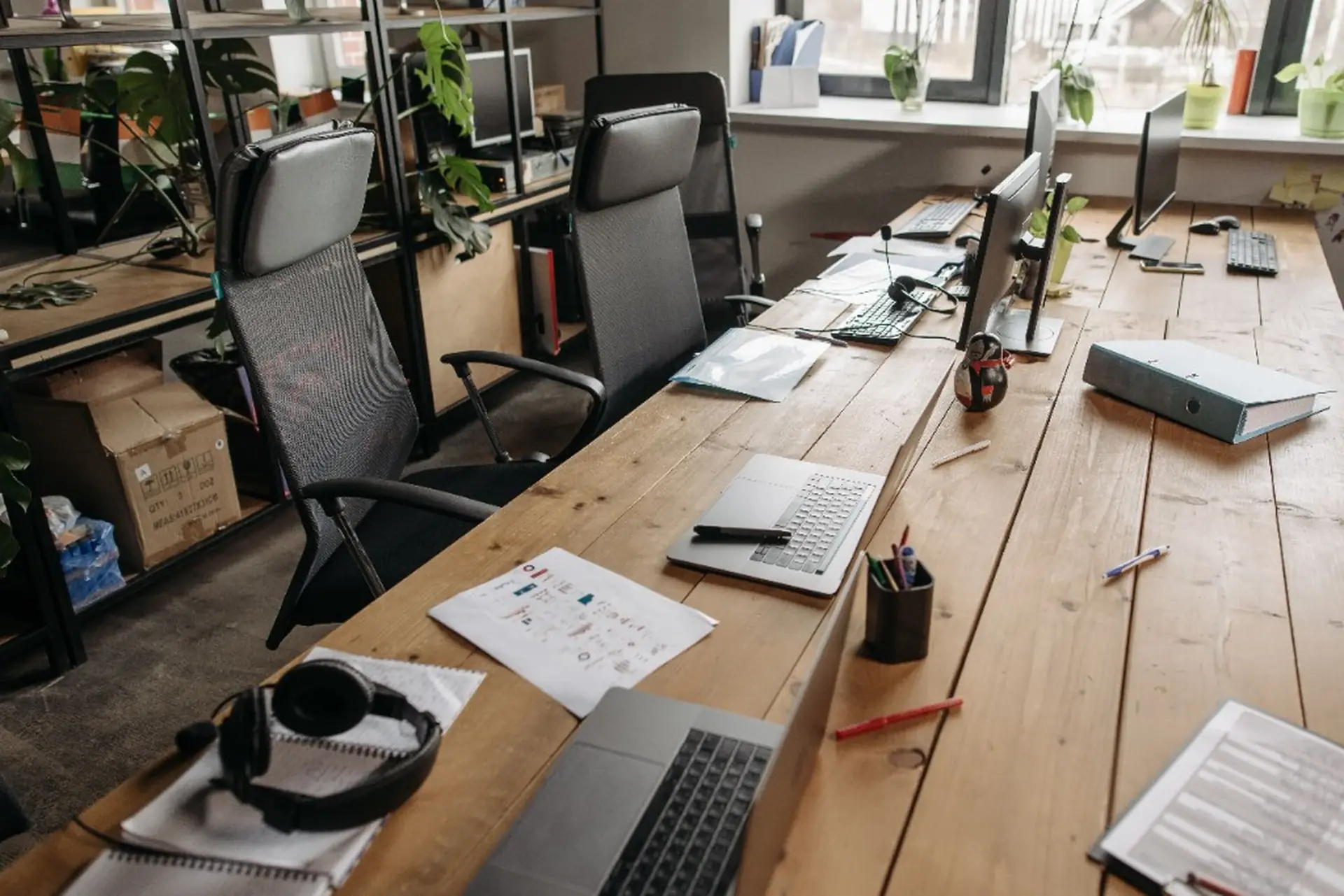 Open-plan office with a long wooden communal desk, workstations and black ergonomic chairs
