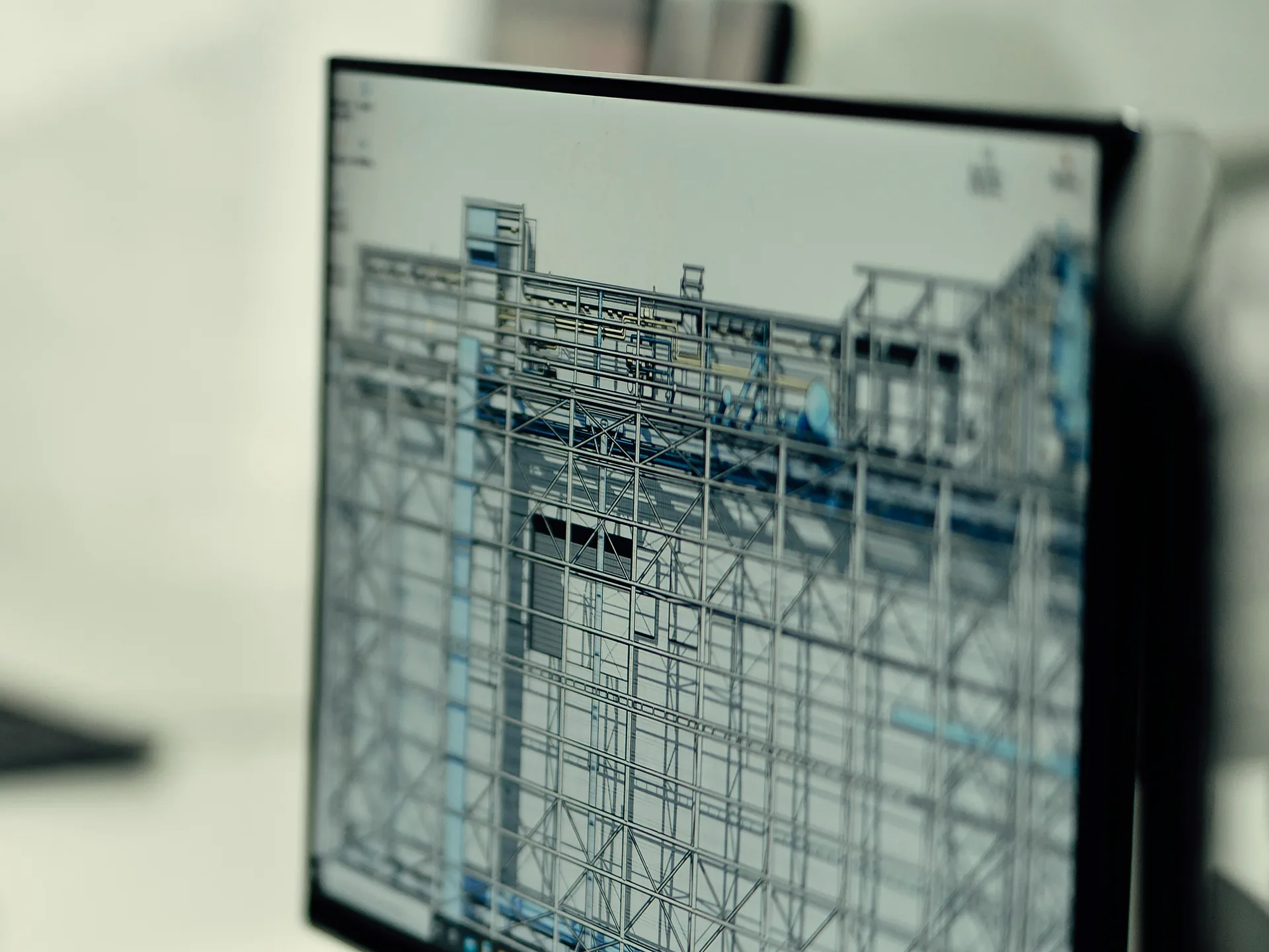 Monitor showing a 3D BIM model of a steel-framed building with MEP pipework