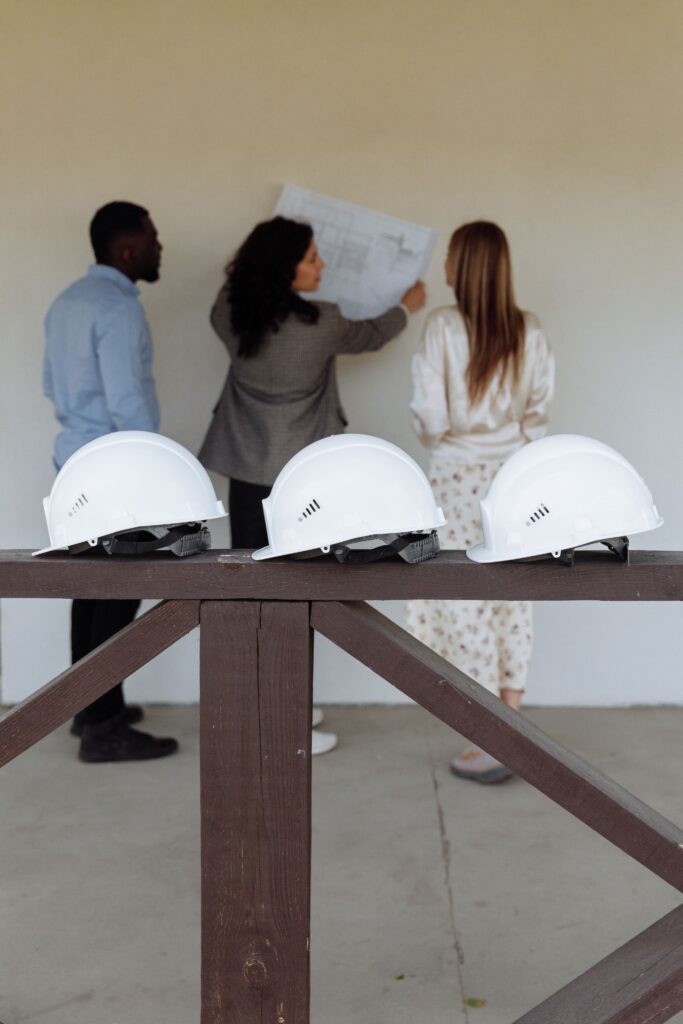 Construction professionals reviewing building plans during a project planning meeting with safety helmets in the foreground.