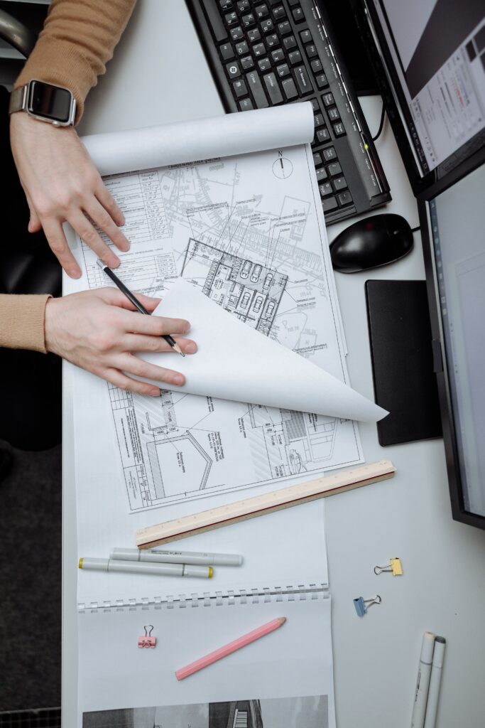 Engineer reviewing construction blueprints on a desk with architectural drawings, computer monitors, and drafting tools