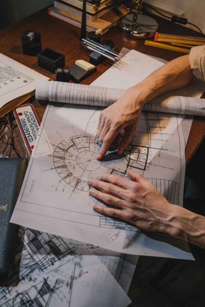 Close-up of a construction drafter reviewing detailed architectural floor plans and technical drawings on a desk with drafting tools and blueprints.