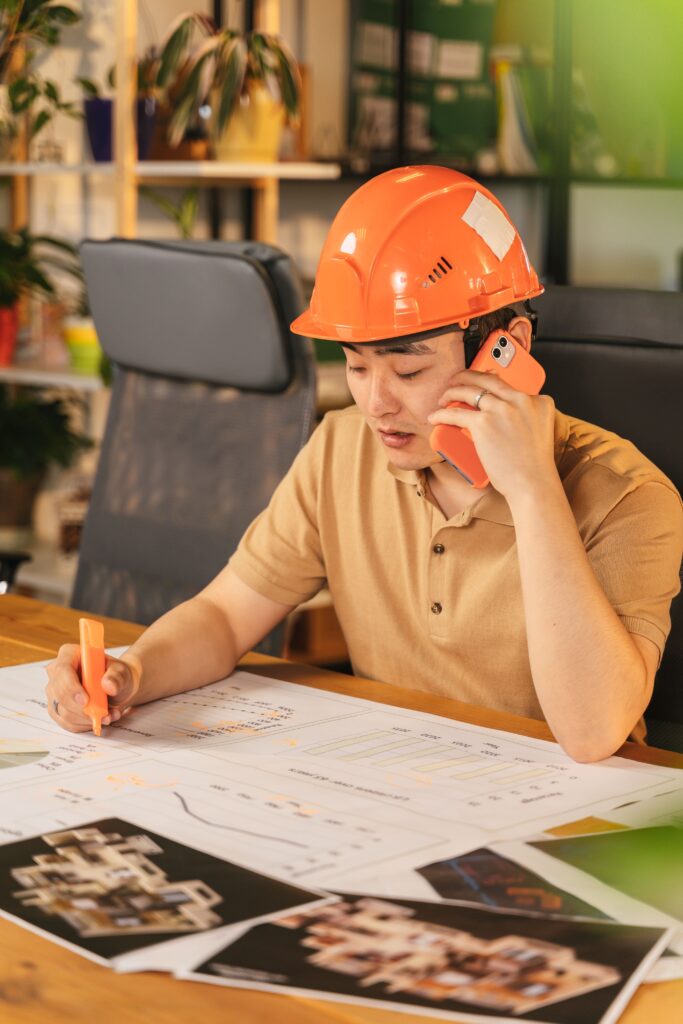 Construction professional reviewing building plans while talking on the phone, highlighting architectural drawings at a desk in a modern office.