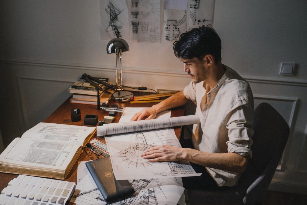 Construction drafter reviewing architectural blueprints and technical drawings at a desk, preparing detailed building plans in a professional workspace.