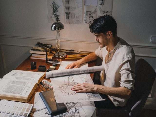 Construction drafter reviewing architectural blueprints and technical drawings at a desk, preparing detailed building plans in a professional workspace.