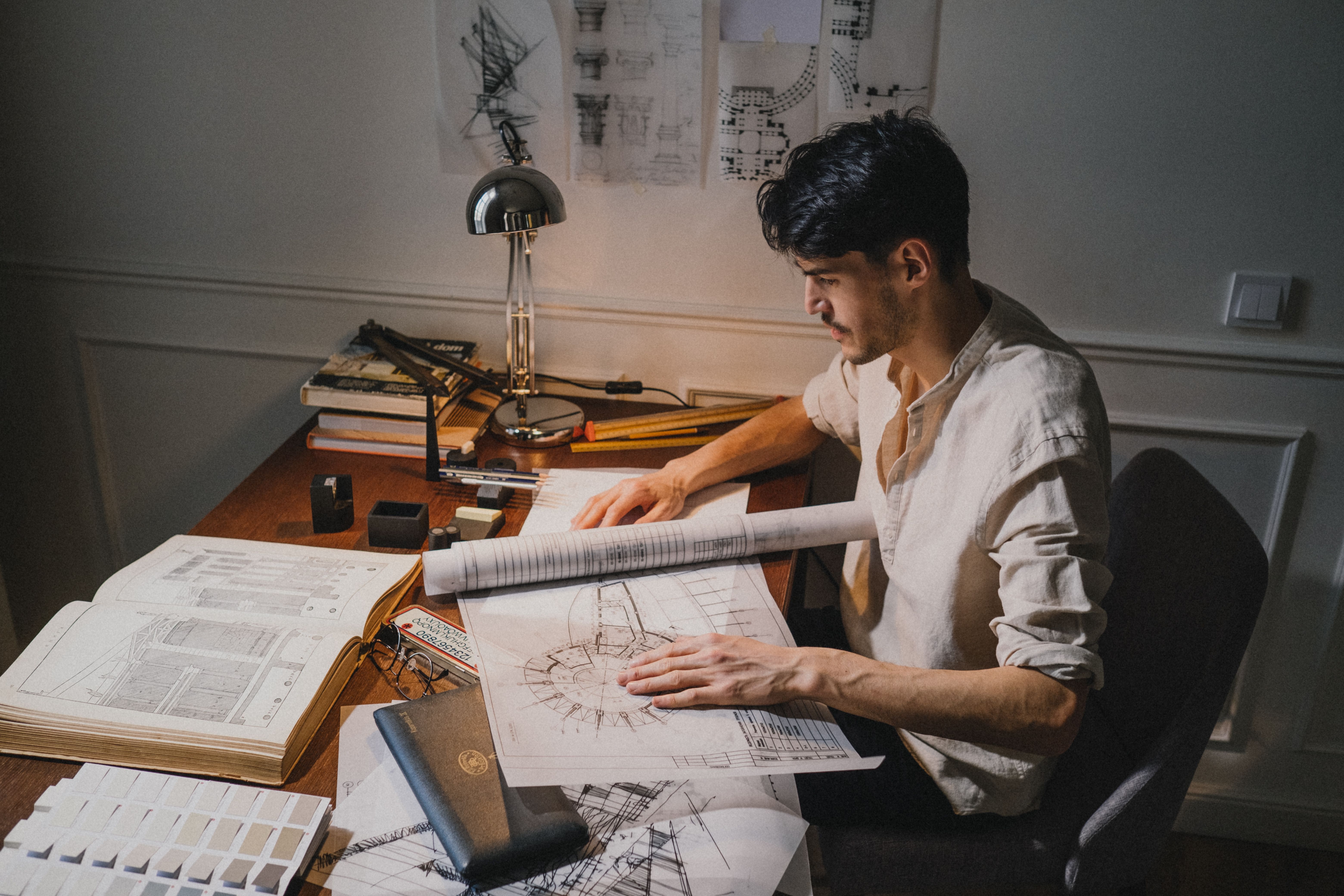 Construction drafter reviewing architectural blueprints and technical drawings at a desk, preparing detailed building plans in a professional workspace.