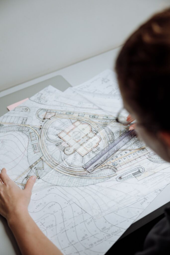 Designer reviewing detailed architectural site plans and construction drawings on paper, using a ruler to measure and analyze project layouts.