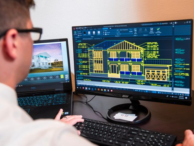 CAD technician designing a residential building in AutoCAD, viewing architectural elevations and technical drafting details on a desktop monitor.