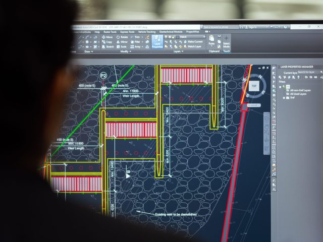 Close-up of a CAD designer reviewing a detailed engineering drawing in AutoCAD Civil 3D, displaying technical construction plans, dimensions, layers, and infrastructure design elements on a computer monitor.