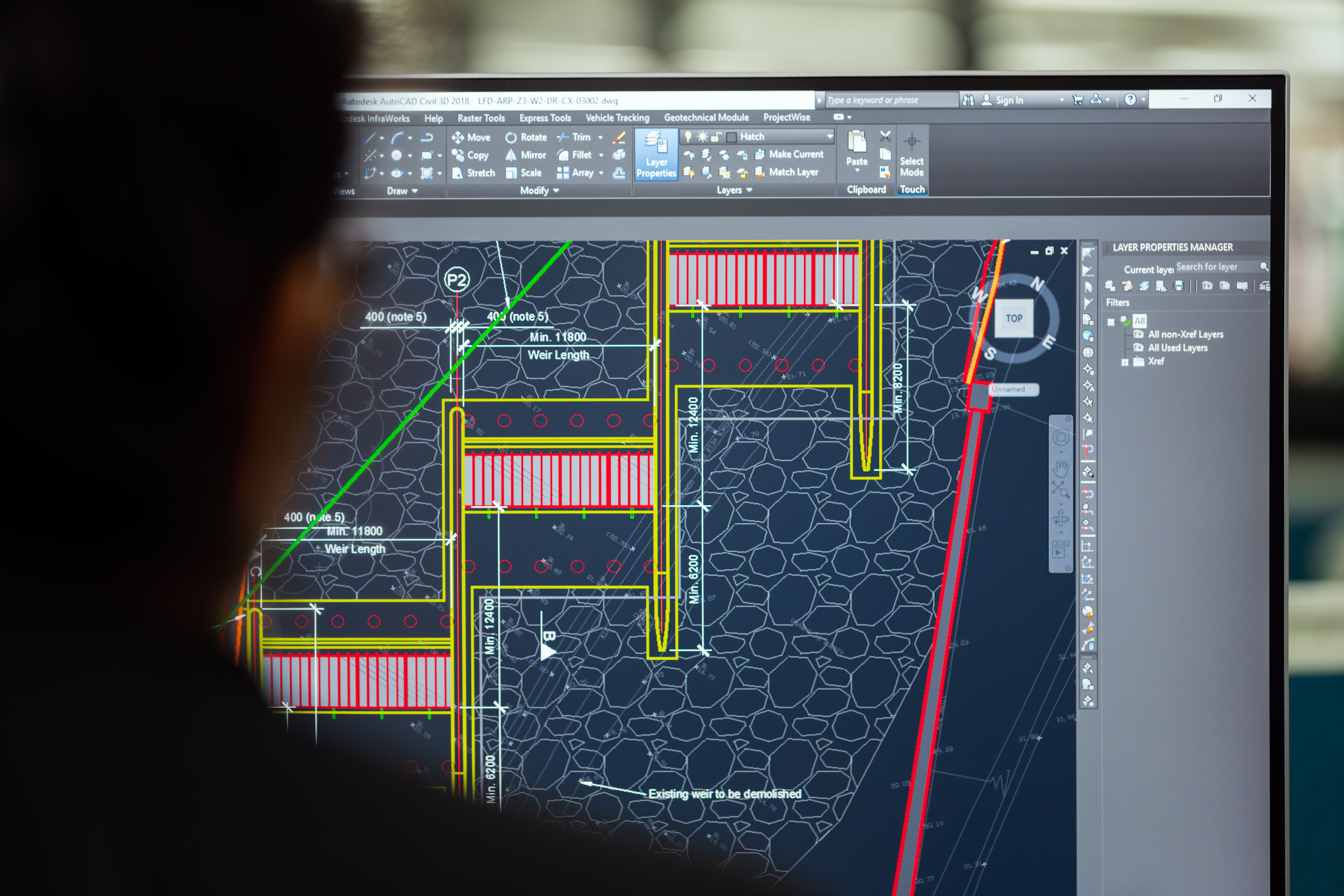 Close-up of a CAD designer reviewing a detailed engineering drawing in AutoCAD Civil 3D, displaying technical construction plans, dimensions, layers, and infrastructure design elements on a computer monitor.