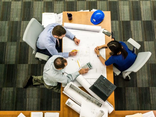 Civil engineering team reviewing construction drawings and project plans around a conference table.