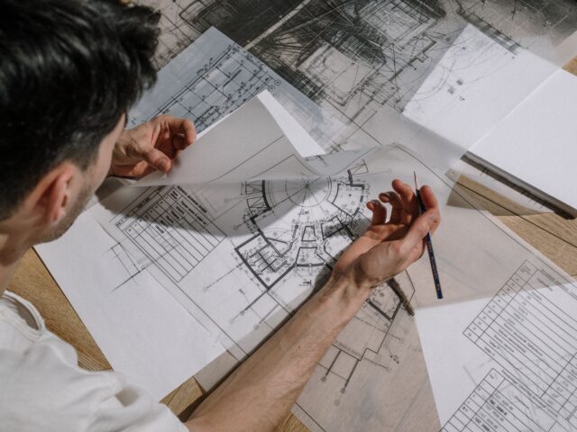 Architect reviewing construction drawings and architectural blueprints on a desk during project planning and design coordination.