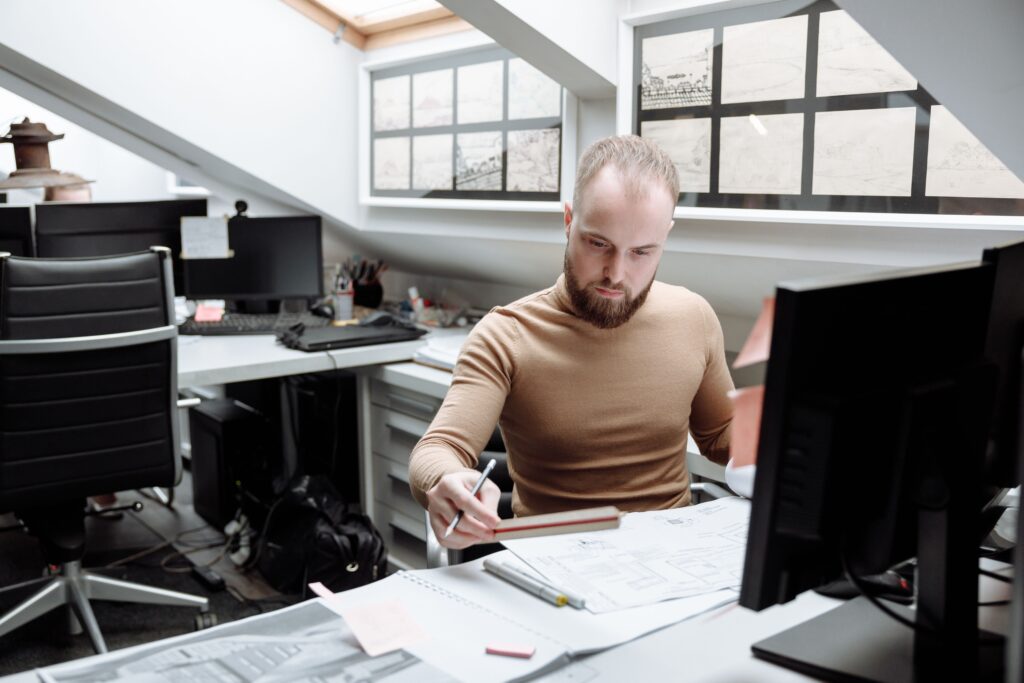 Construction professional reviewing project drawings and technical documents at an office desk.