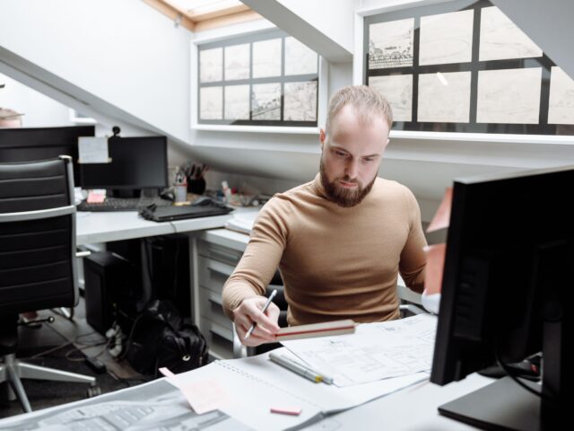 Construction professional reviewing project drawings and technical documents at an office desk.
