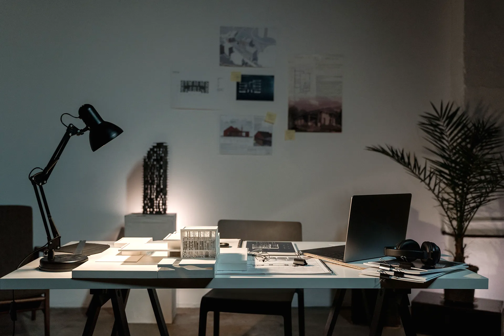Architecture and engineering office desk with a laptop, drawing sets, building models, and plans pinned to the wall