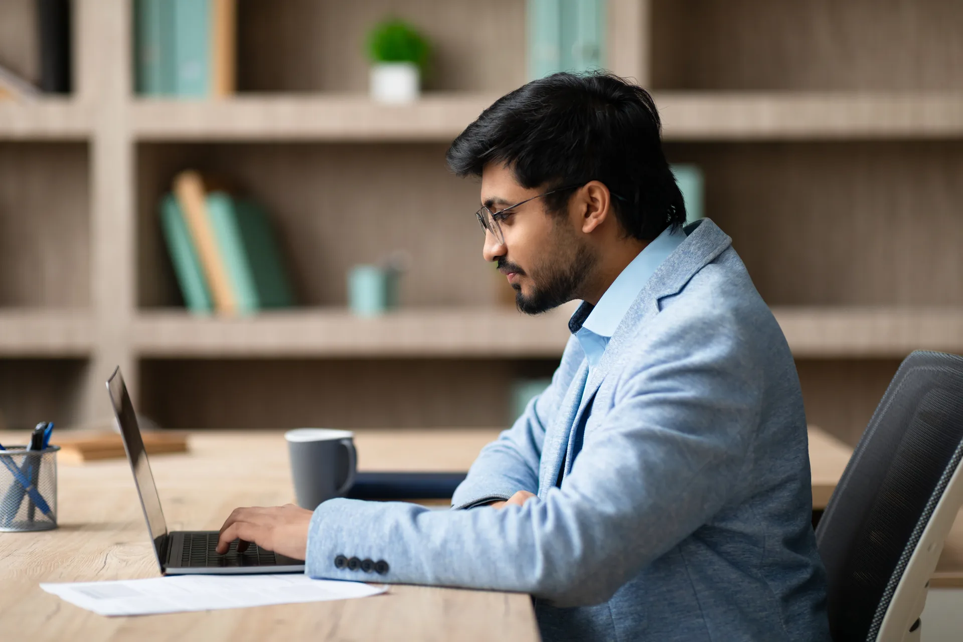 Assistant in glasses typing emails on a laptop at an office desk, managing the studio inbox and client messages