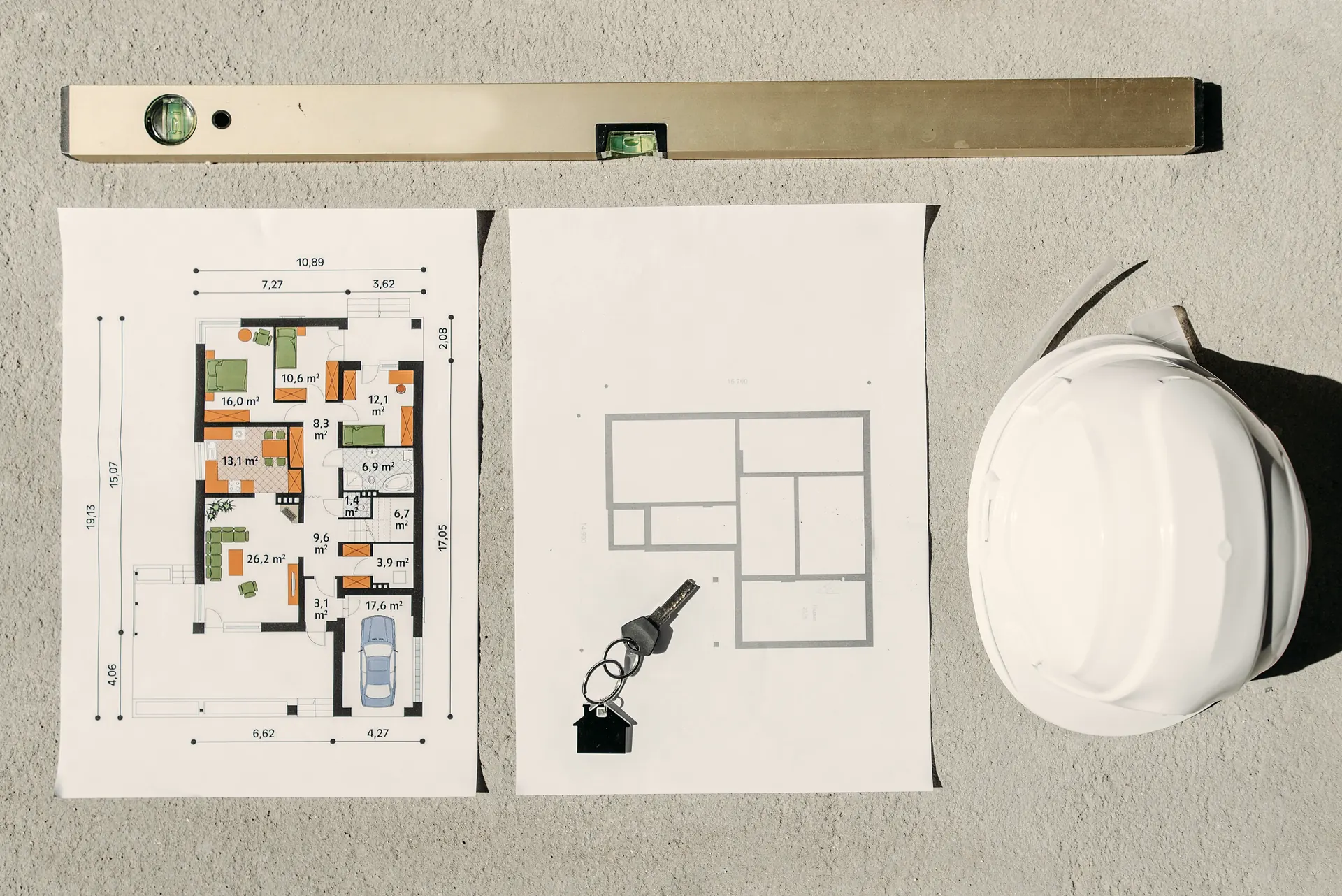 Overhead view of printed floor plans, a spirit level, a white hard hat and a set of house keys, the handover stage of a construction project