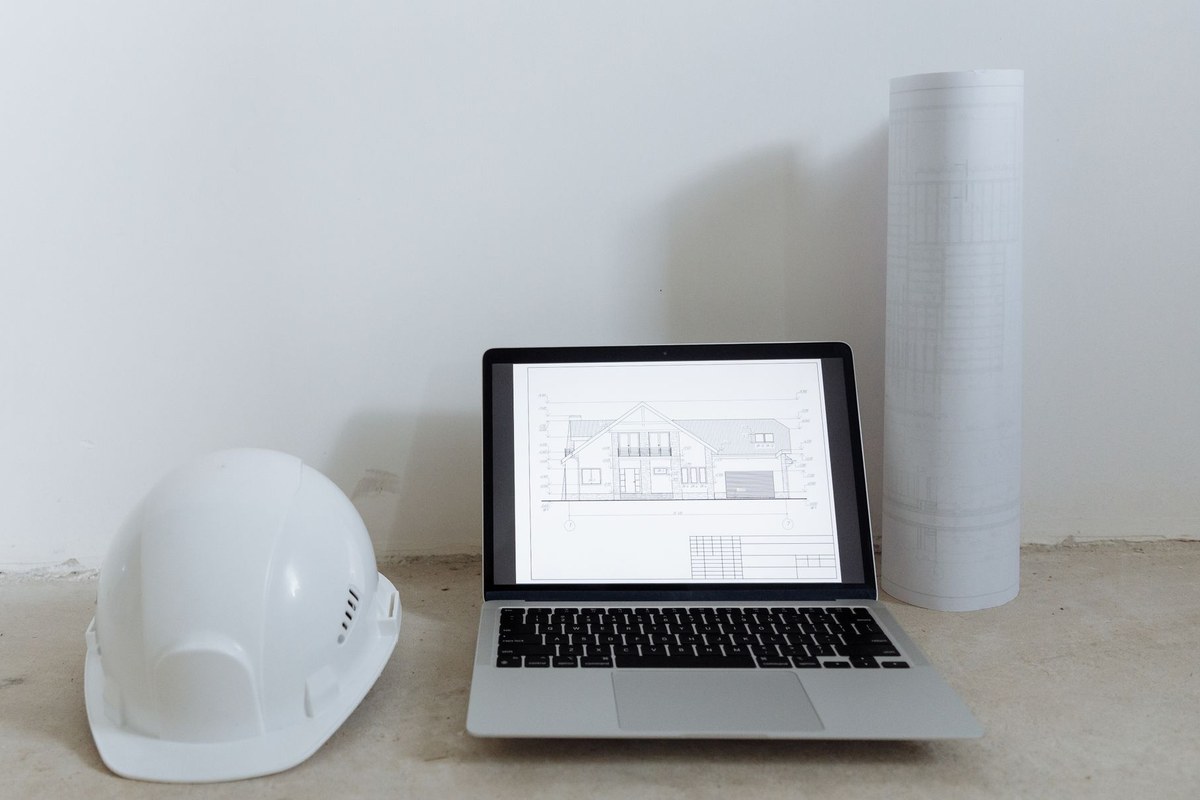 Laptop showing a building elevation drawing beside a hard hat and rolled construction plans