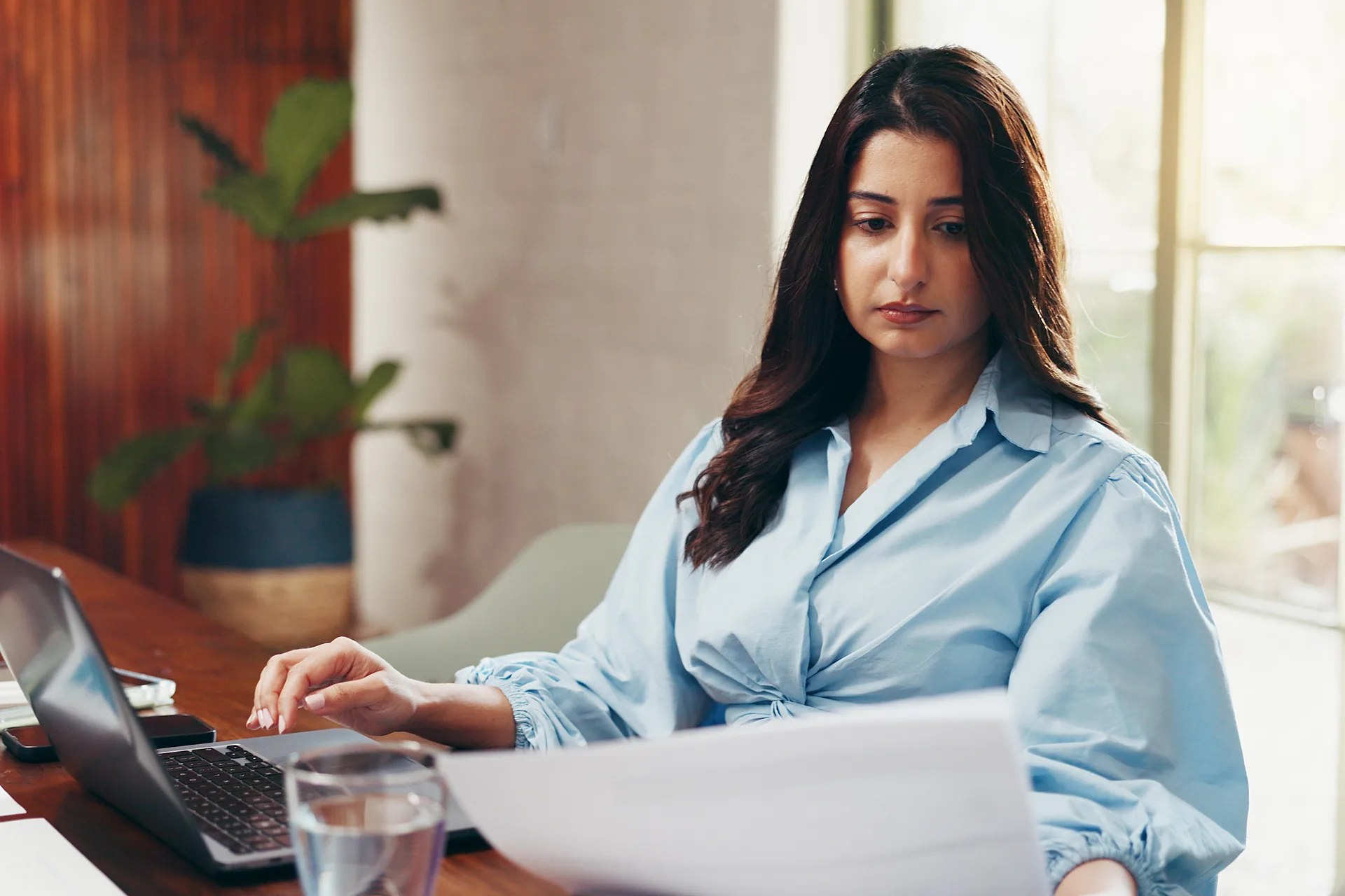 Office administrator reviewing printed invoices and updating billing records on a laptop