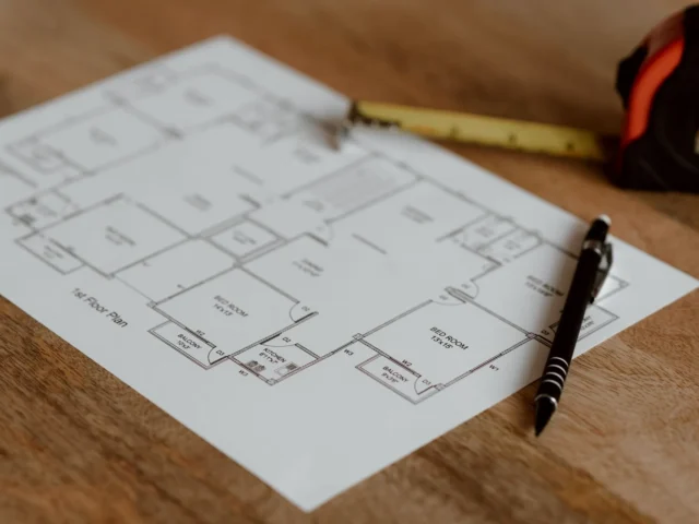 Printed floor plan on a wooden desk with a pen and tape measure, ready for a quantity takeoff