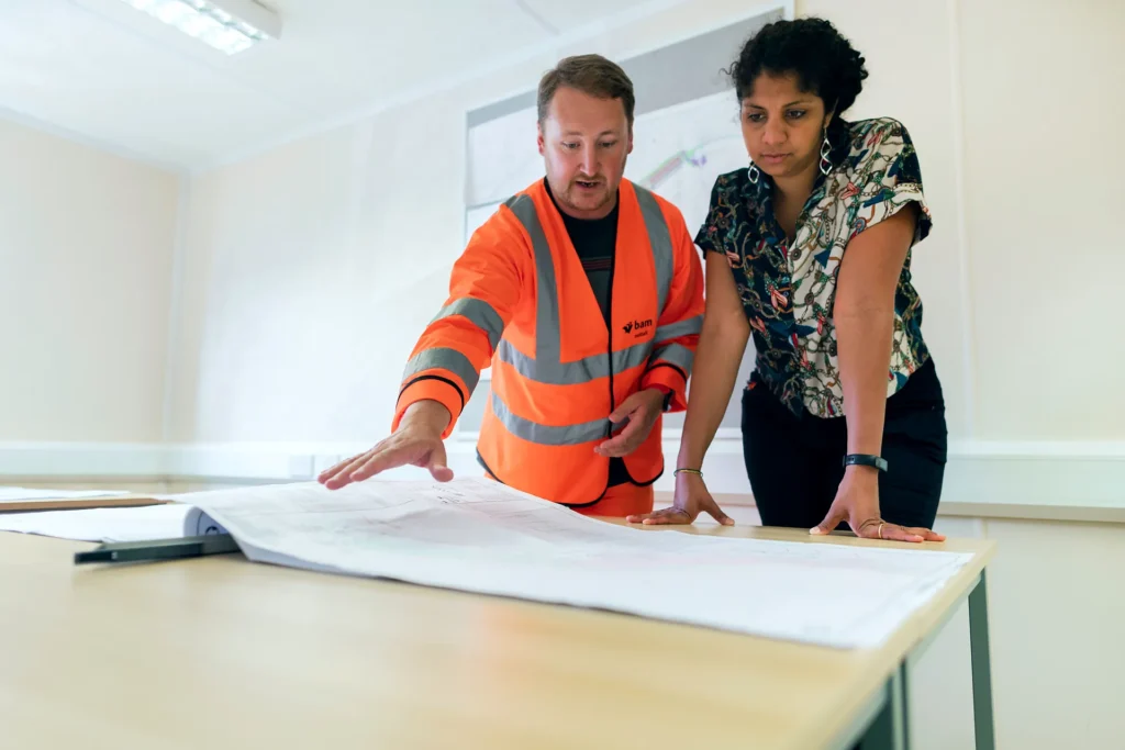 South Asian project coordinator reviewing a drawing set with a site engineer in a construction project office