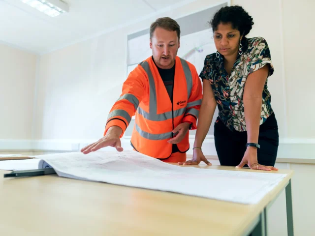 South Asian project coordinator reviewing a drawing set with a site engineer in a construction project office