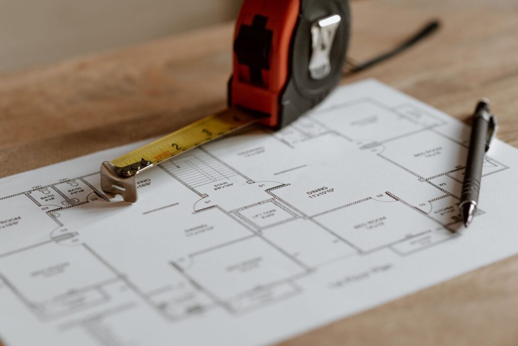 Floor plan with a tape measure and pen, the kind of quantity takeoff work a dedicated remote estimator handles